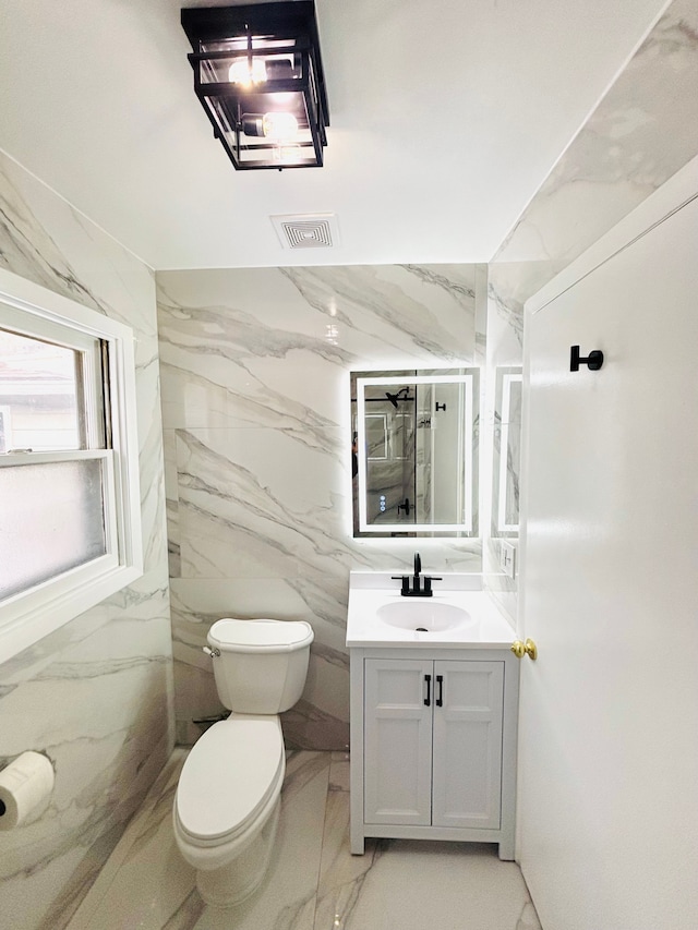 bathroom featuring visible vents, toilet, stone wall, marble finish floor, and vanity