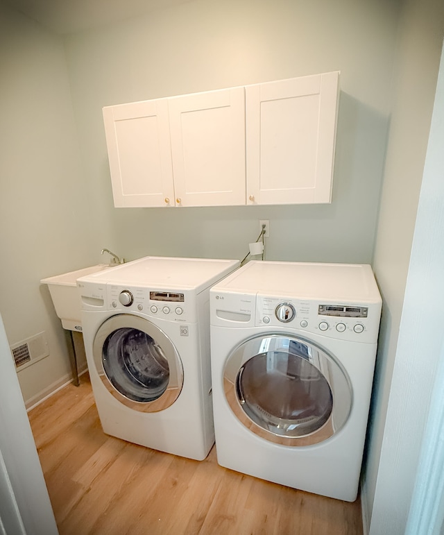 laundry area with cabinets, washing machine and dryer, and light wood-type flooring