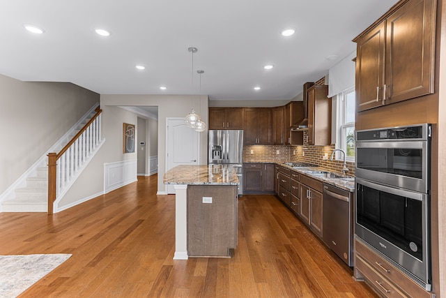 kitchen featuring decorative light fixtures, a center island, hardwood / wood-style flooring, stainless steel appliances, and light stone countertops