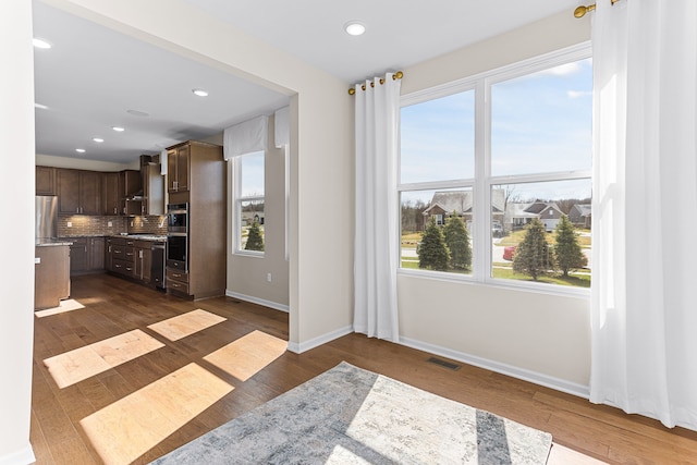 kitchen featuring dark wood-type flooring, dark brown cabinets, appliances with stainless steel finishes, decorative backsplash, and wall chimney range hood