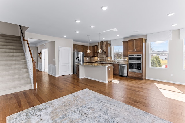 kitchen with stainless steel appliances, light stone countertops, a kitchen island, and decorative light fixtures