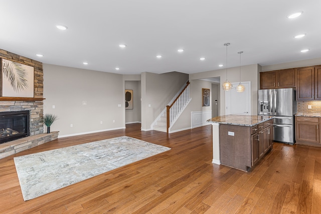 kitchen featuring a stone fireplace, decorative light fixtures, a center island, light stone counters, and stainless steel fridge with ice dispenser