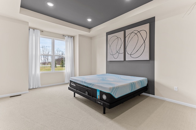 bedroom with light colored carpet and a tray ceiling