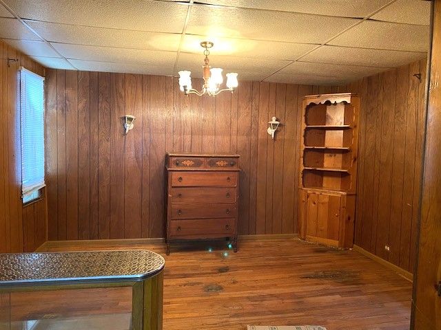 interior space with a paneled ceiling, hardwood / wood-style floors, a notable chandelier, and wooden walls