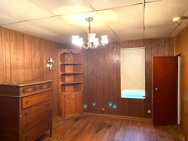 unfurnished room with dark hardwood / wood-style flooring, a drop ceiling, an inviting chandelier, and wood walls