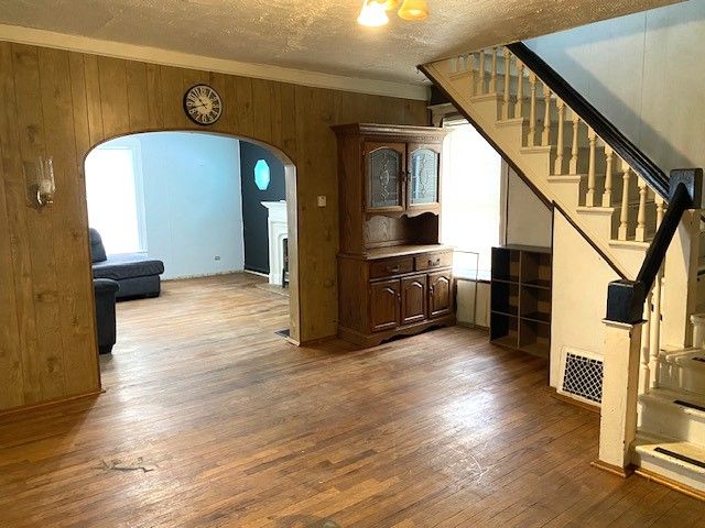 unfurnished living room with ornamental molding, hardwood / wood-style floors, a textured ceiling, and wood walls