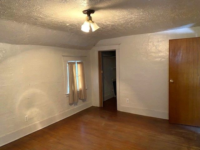 spare room featuring vaulted ceiling, dark hardwood / wood-style floors, and a textured ceiling