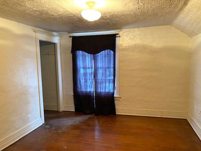 unfurnished room with dark hardwood / wood-style flooring, lofted ceiling, and a textured ceiling