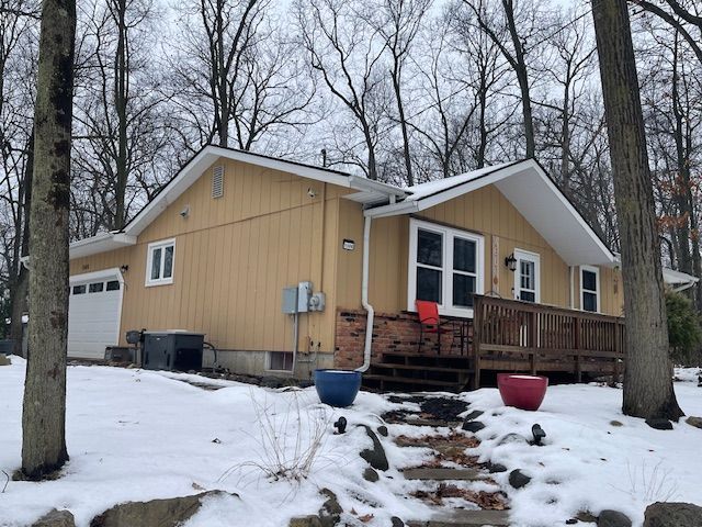 snow covered property with a garage and central AC unit