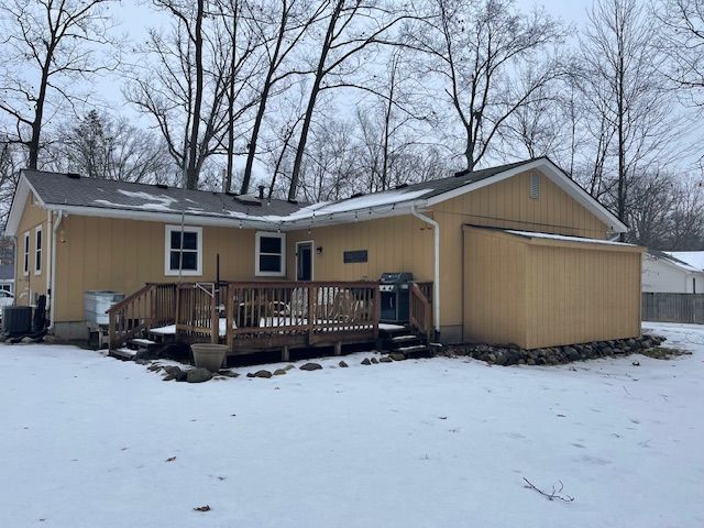 snow covered back of property with a wooden deck and central AC