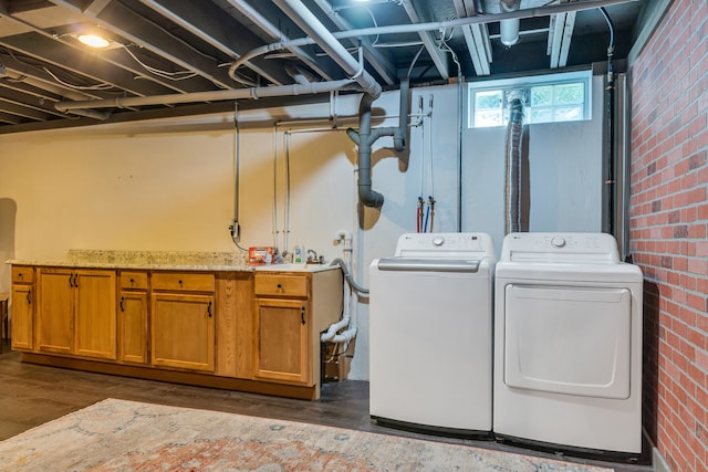 laundry room featuring cabinets, dark hardwood / wood-style flooring, brick wall, and washer and clothes dryer