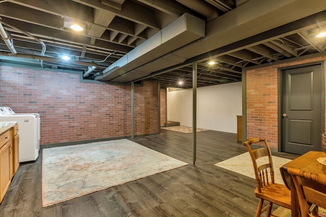 basement featuring brick wall, dark hardwood / wood-style flooring, and washer and clothes dryer