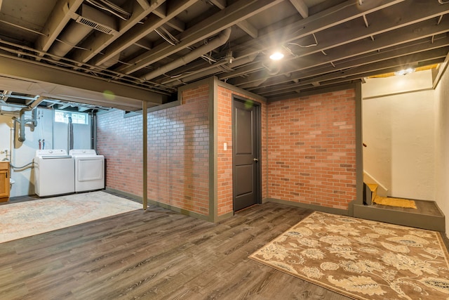 basement featuring hardwood / wood-style flooring, washing machine and clothes dryer, and brick wall