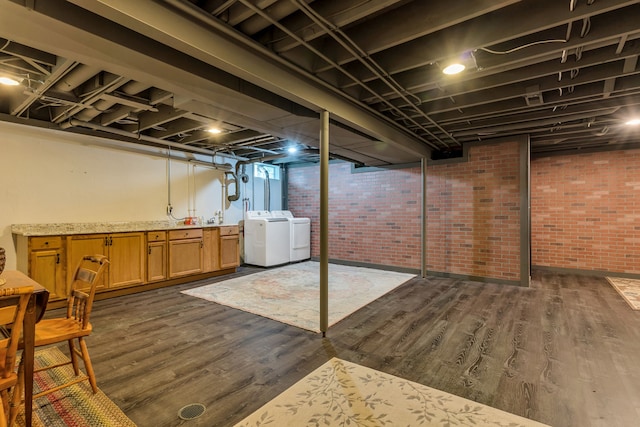 basement with brick wall, separate washer and dryer, and dark hardwood / wood-style floors