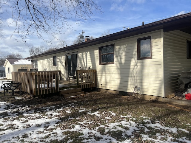 snow covered back of property with a wooden deck