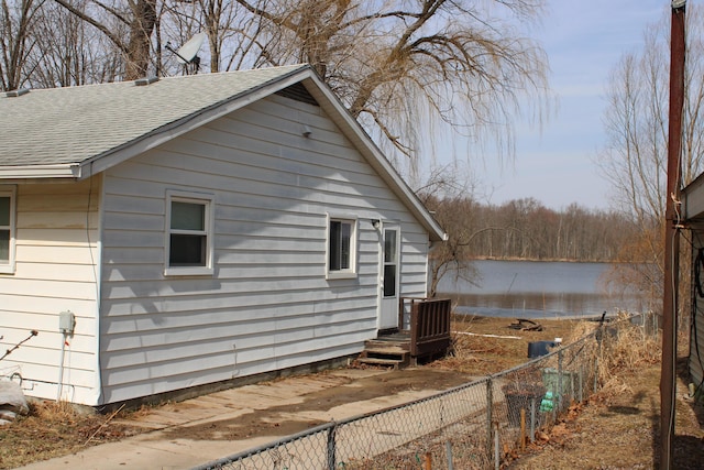 view of side of home featuring fence, a water view, and roof with shingles