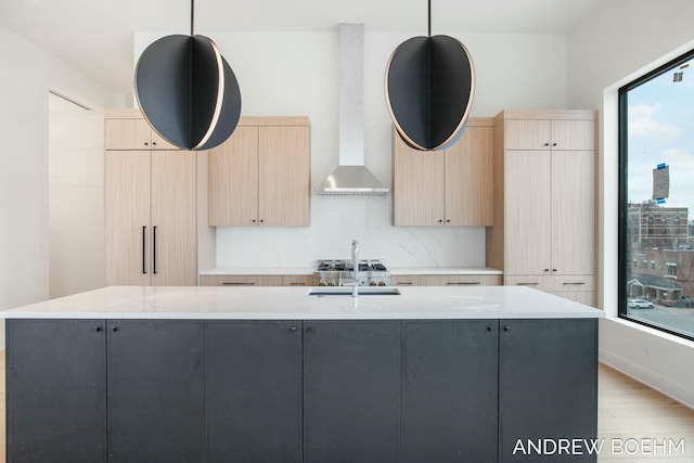 kitchen featuring a center island with sink, pendant lighting, light brown cabinetry, and wall chimney exhaust hood