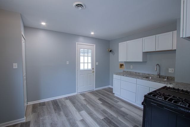 kitchen featuring gas stove, sink, white cabinetry, light stone counters, and light wood-type flooring