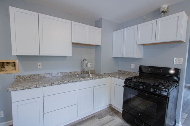 kitchen with white cabinetry, sink, light hardwood / wood-style floors, and black gas stove