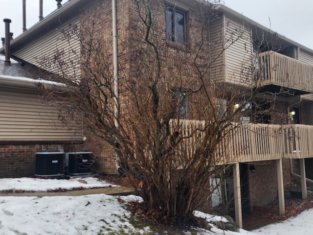 snow covered property featuring cooling unit, a balcony, and a deck