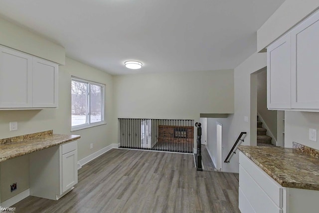 kitchen with white cabinetry, light stone counters, built in desk, and light hardwood / wood-style floors