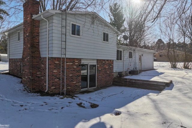 snow covered back of property featuring central AC unit