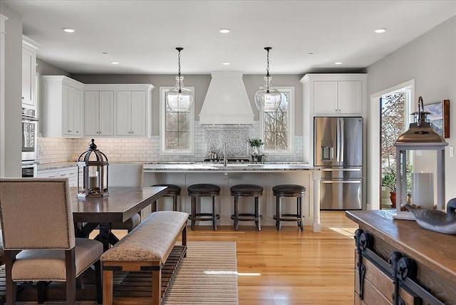 kitchen featuring pendant lighting, stainless steel fridge, white cabinetry, a kitchen breakfast bar, and custom range hood