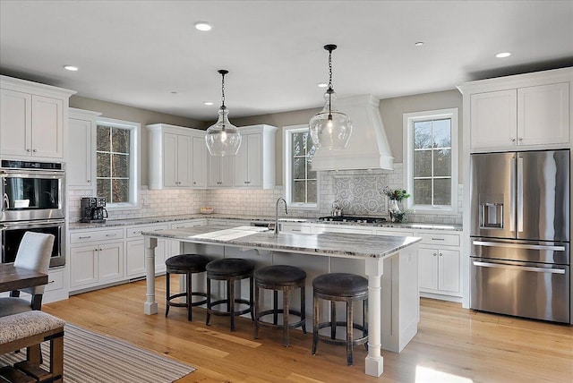 kitchen featuring white cabinetry, a center island with sink, custom exhaust hood, and appliances with stainless steel finishes