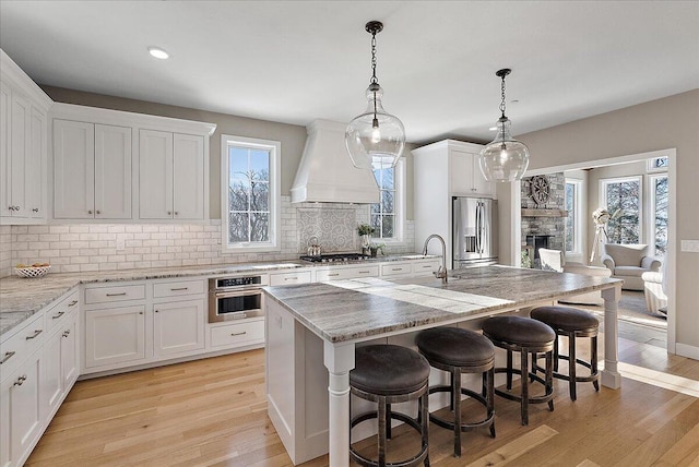 kitchen with white cabinetry, stainless steel appliances, a kitchen island with sink, and custom exhaust hood