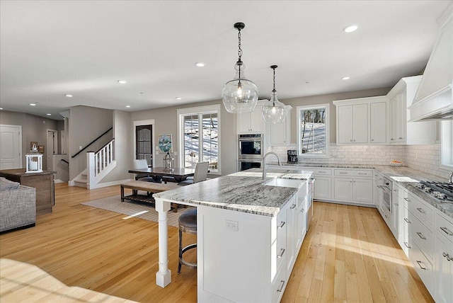 kitchen with light hardwood / wood-style flooring, decorative light fixtures, a center island with sink, and white cabinets