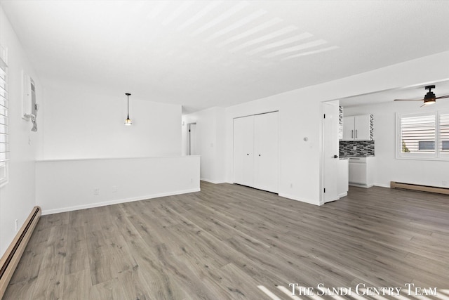 unfurnished living room with wood-type flooring, ceiling fan, and baseboard heating