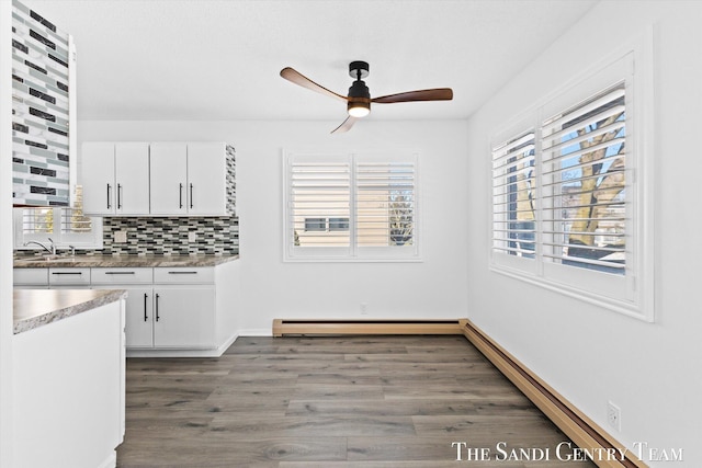 kitchen featuring sink, white cabinetry, baseboard heating, a healthy amount of sunlight, and backsplash