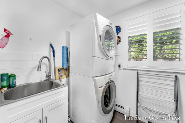 clothes washing area with cabinets, stacked washing maching and dryer, sink, and baseboard heating