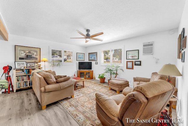 living room with a wall mounted air conditioner, a textured ceiling, ceiling fan, and light wood-type flooring