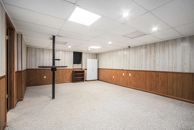 basement featuring light colored carpet, a drop ceiling, and wood walls