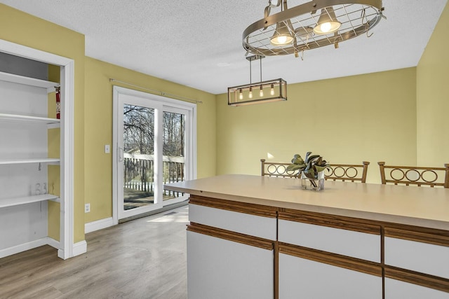 kitchen featuring white cabinetry, decorative light fixtures, a textured ceiling, and light hardwood / wood-style flooring