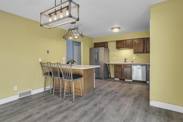 kitchen with appliances with stainless steel finishes, decorative light fixtures, wood-type flooring, a kitchen breakfast bar, and kitchen peninsula