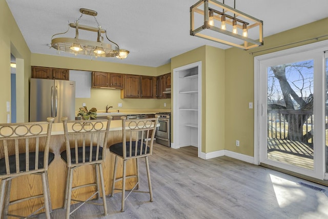 kitchen with appliances with stainless steel finishes, sink, a breakfast bar area, hanging light fixtures, and light hardwood / wood-style flooring