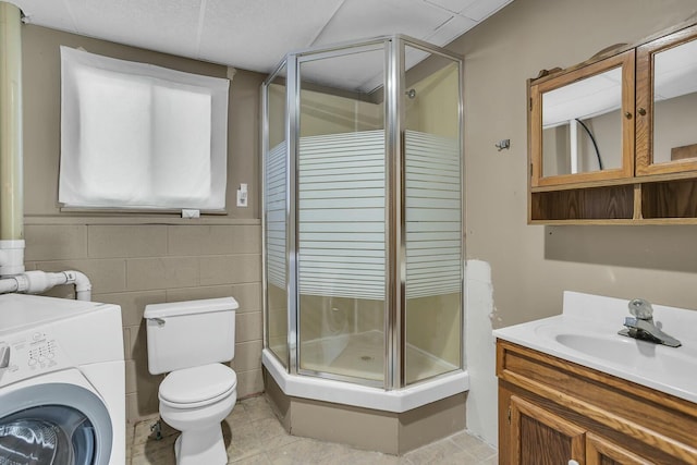 bathroom with a shower with shower door, washer / dryer, tile walls, vanity, and toilet