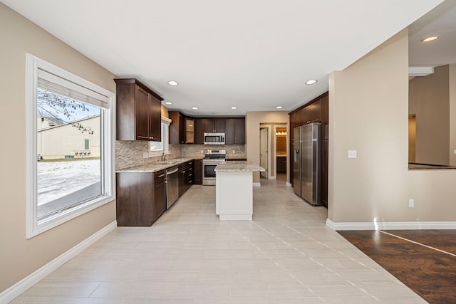 kitchen with dark brown cabinetry, tasteful backsplash, appliances with stainless steel finishes, a kitchen island, and light stone countertops