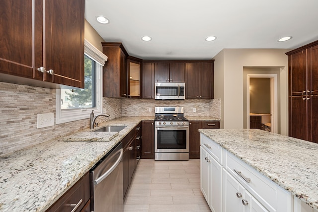 kitchen featuring appliances with stainless steel finishes, sink, white cabinets, dark brown cabinetry, and light stone counters