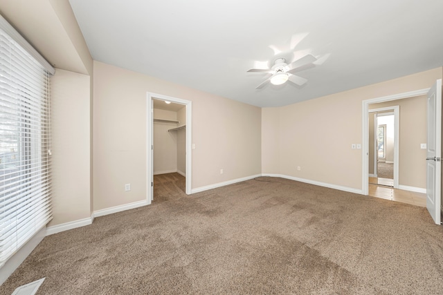 unfurnished bedroom with ceiling fan, a walk in closet, carpet floors, and multiple windows