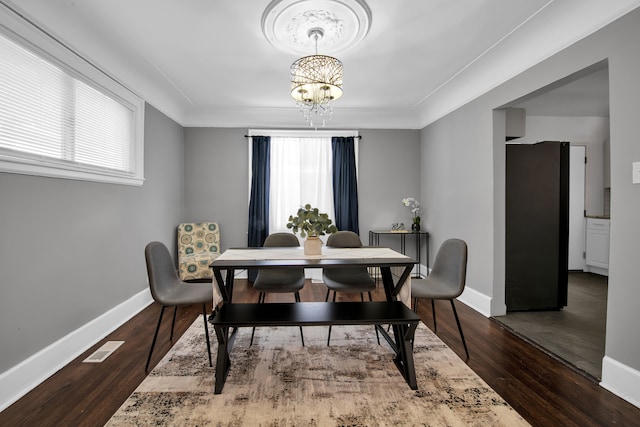 dining space with dark wood-type flooring, ornamental molding, a wealth of natural light, and a notable chandelier