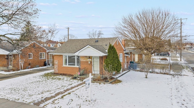 bungalow featuring brick siding, a shingled roof, and fence