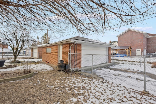 view of snow covered exterior featuring a garage, brick siding, and fence