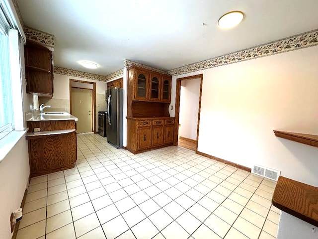 kitchen featuring visible vents, open shelves, baseboards, freestanding refrigerator, and a sink