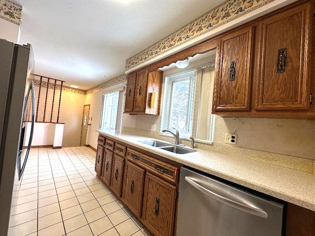 kitchen with brown cabinetry, light tile patterned flooring, a sink, light countertops, and appliances with stainless steel finishes