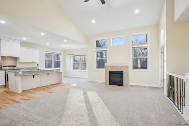 unfurnished living room with sink, high vaulted ceiling, a tile fireplace, light colored carpet, and ceiling fan with notable chandelier