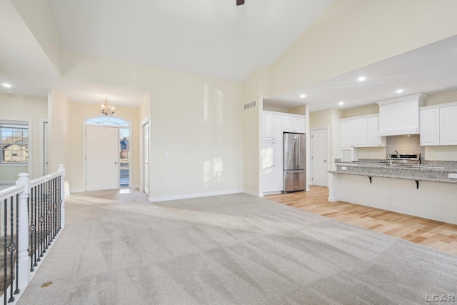 unfurnished living room featuring lofted ceiling, sink, light colored carpet, and an inviting chandelier