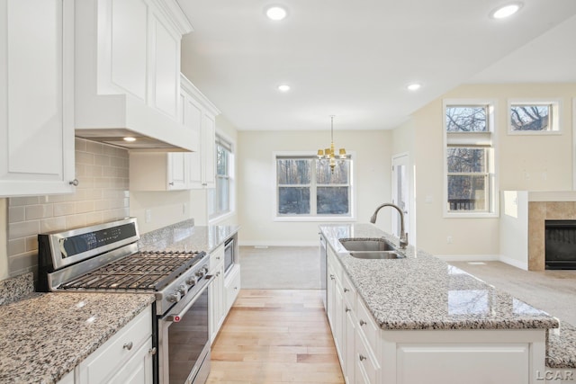 kitchen featuring white cabinetry, an island with sink, sink, and stainless steel gas range